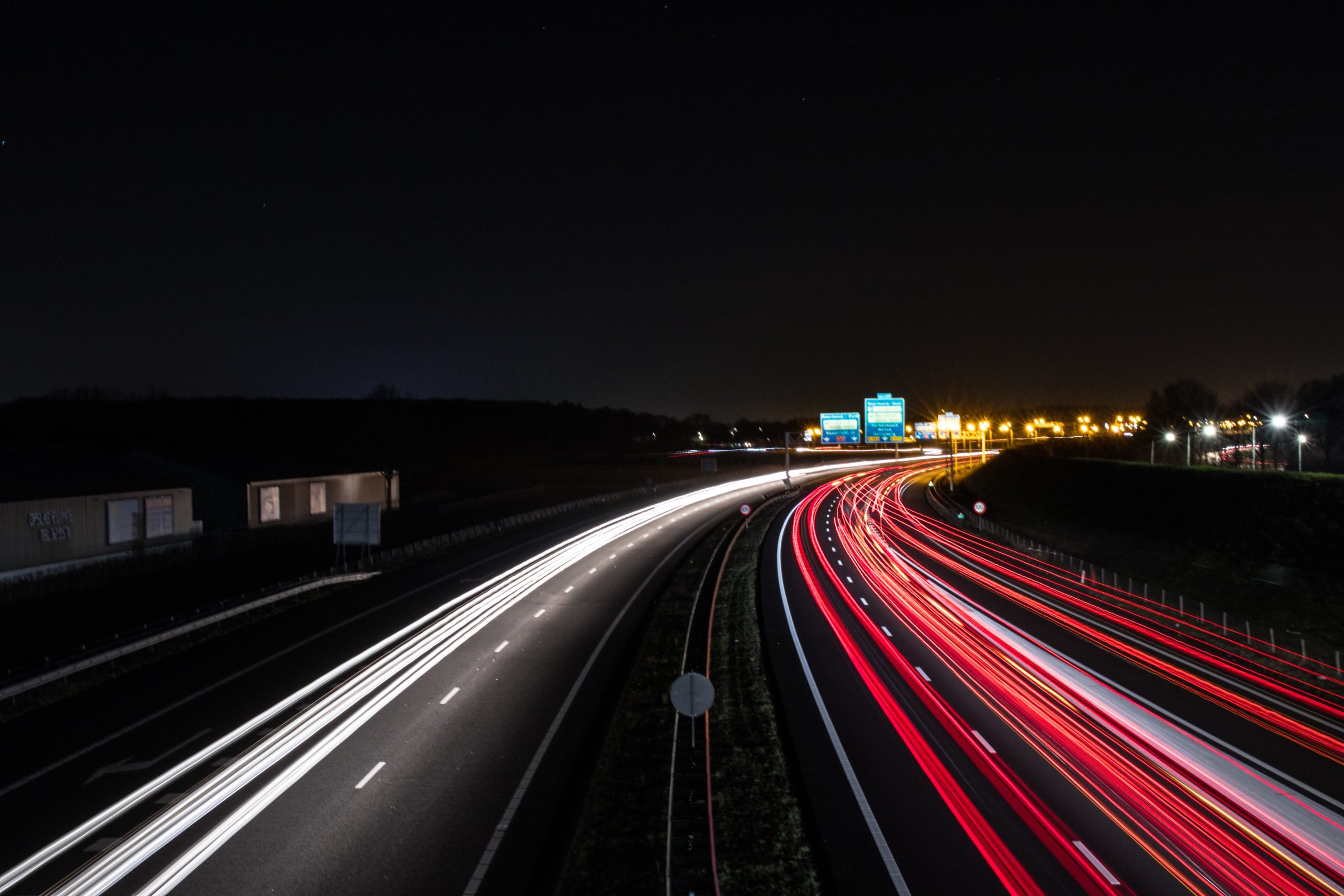 A long exposure photo of a New Jersey highway at night captures white and red light trails from vehicles. The road curves slightly with overhead signs in the distance. The dark sky looms over this serene yet cautionary scene, as a reminder of the potential for auto accidents on these paths.
