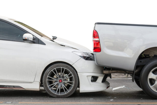 A white sedan has rear-ended a light gray pickup truck, causing visible damage to both vehicles. Rear-end accidents like this often raise questions about car accident liability, especially regarding the back driver's fault.